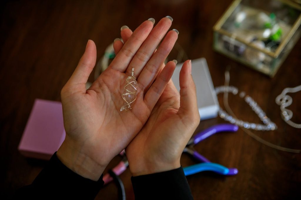 Close-up of hands presenting a handmade silver wire pendant with jewelry tools on a wooden table.